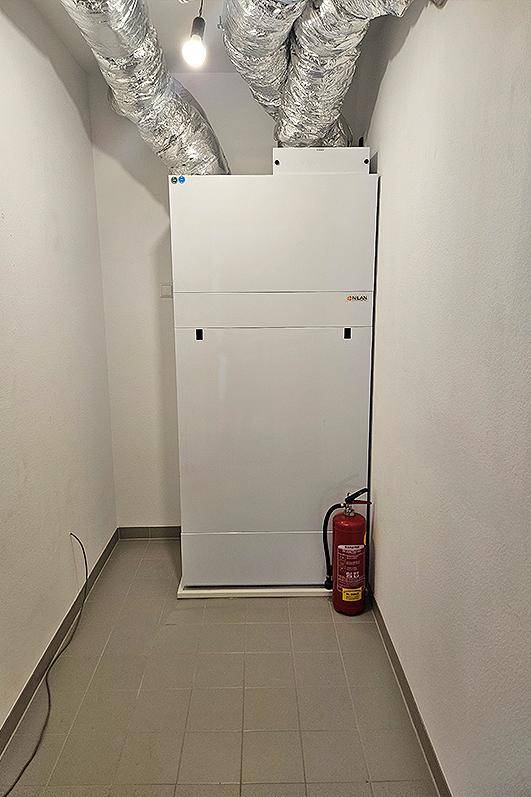 Technikraum mit Lüftungsanlage, sichtbaren Lüftungsrohren und einem Feuerlöscher für die Sicherheit.