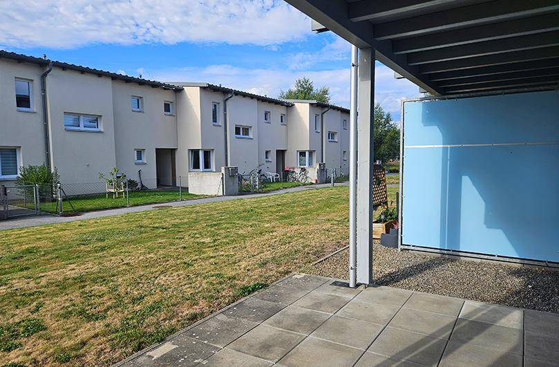 Aussicht von der Terrasse über eine grüne Rasenfläche auf eine Reihe moderner Reihenhäuser.