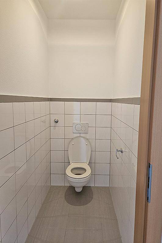 Kleines, funktionales WC mit weißen Wandfliesen, grauen Bodenfliesen und wandhängendem WC.
