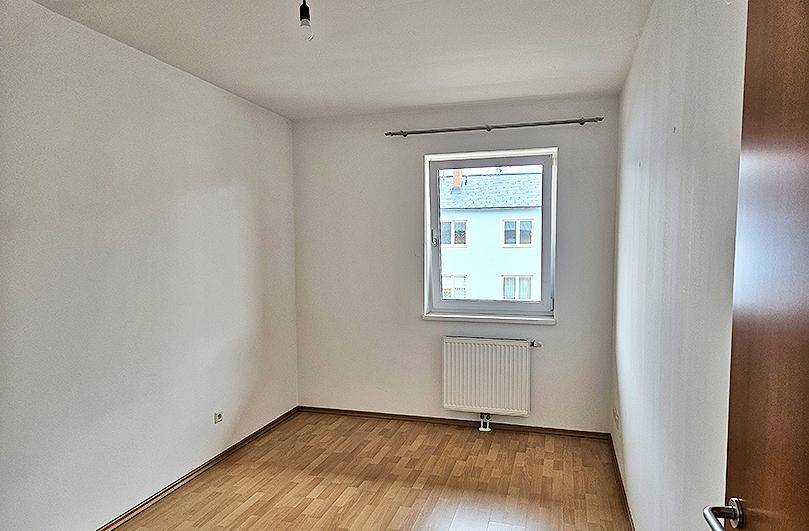 Schlafzimmer mit Laminatboden, weißen Wänden und einem Fenster, das einen Blick nach draußen bietet.