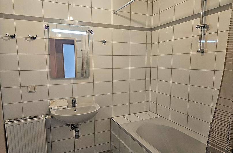 Gefliestes Badezimmer mit Badewanne, Waschbecken und einem Spiegel, typisch für die 80er Jahre.
