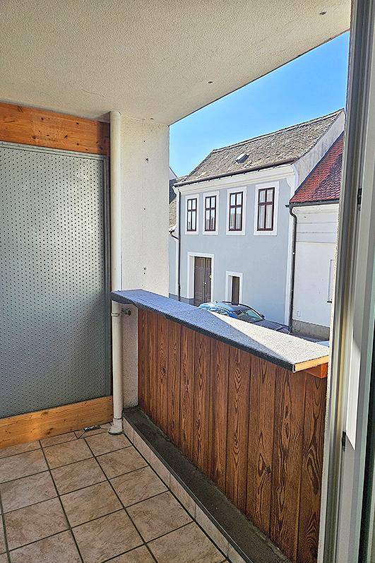 Kleiner Balkon mit Fliesenboden und Holzbrüstung, bietet einen Blick auf die umliegenden Gebäude.
