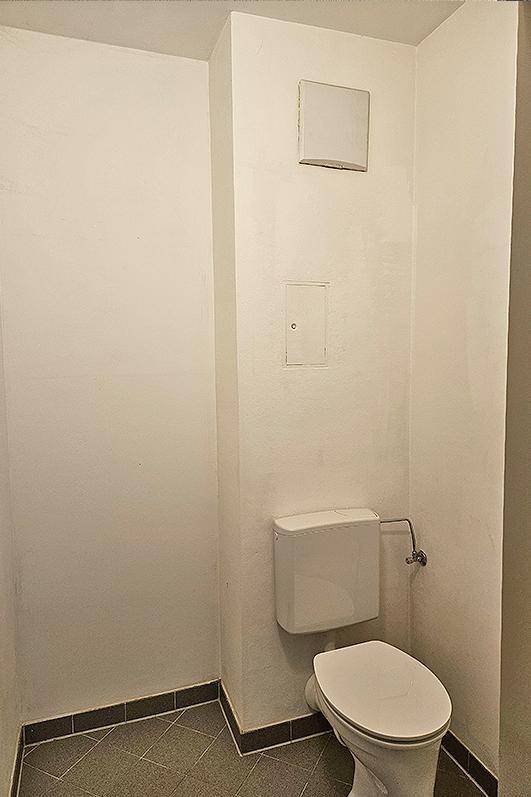 Separates WC mit wandhängender Toilette und grauen Bodenfliesen in einem kleinen Raum.
