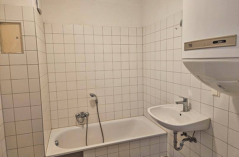 Gefliestes Badezimmer mit Badewanne, Duscharmatur, Waschbecken und Boiler.