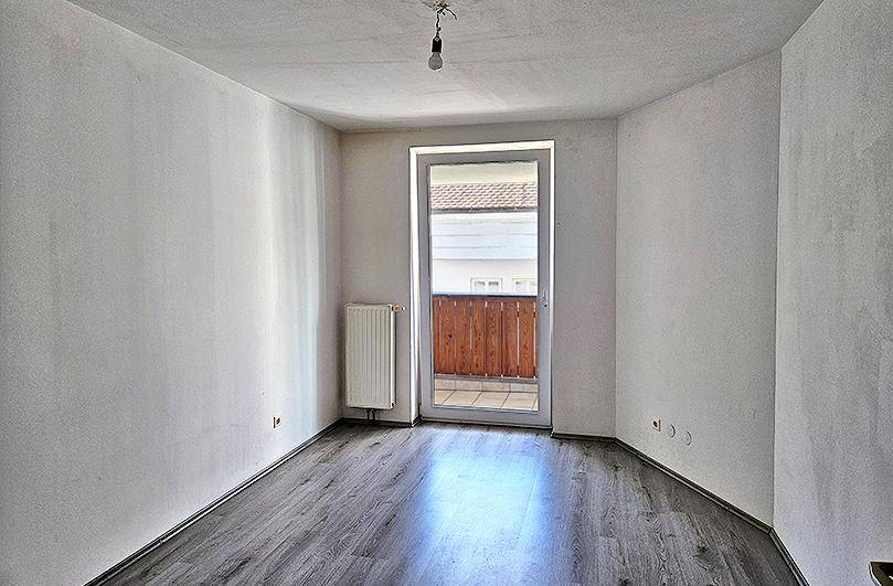 Helles Schlafzimmer mit Laminatboden, Heizkörper und direktem Zugang zum Balkon.