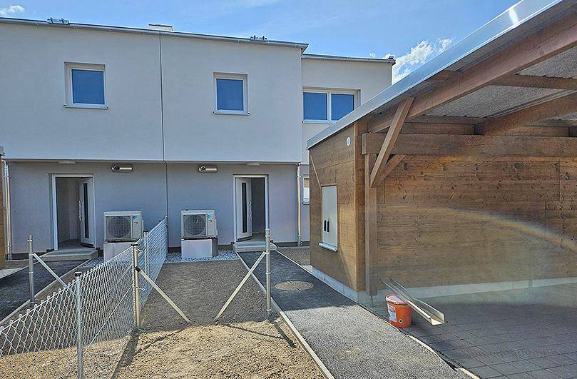 Außenansicht eines Neubaus mit mehreren Wohneinheiten, Klimaanlagen und einem Holzcarport.