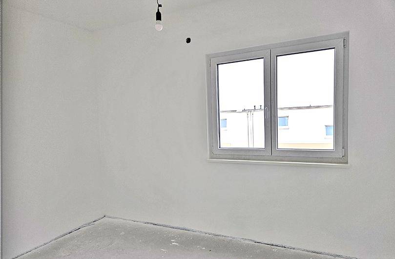 Helles Zimmer im Rohbau mit weiß gestrichenen Wänden und einem Fenster mit Blick auf Nachbargebäude.