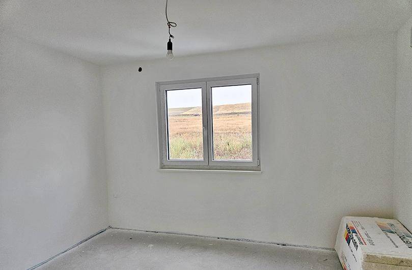 Rohbauzimmer mit weiß gestrichenen Wänden und einem Fenster, das einen Blick auf die Landschaft bietet.