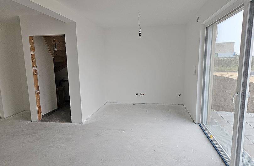 Unfertiger Wohnbereich mit viel Tageslicht und direktem Zugang zur Terrasse oder zum Garten.