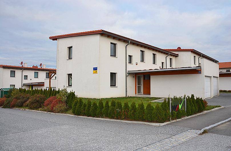 Modernes Reihenhaus mit weißer Fassade, Satteldach und gepflegtem Vorgarten von der Straße aus.