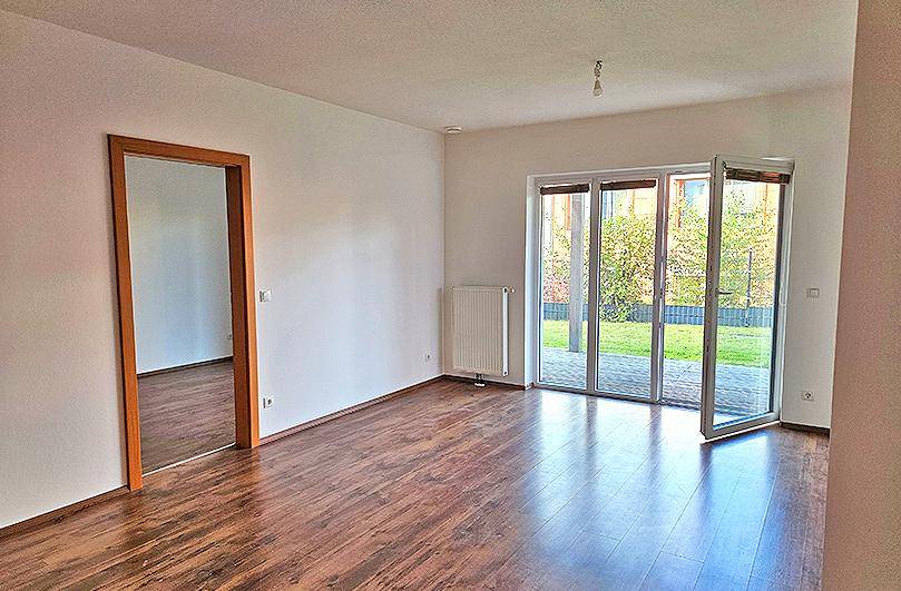 Geräumiger Wohnbereich mit Laminatboden und großen Glasfenstern, die zum Garten führen.