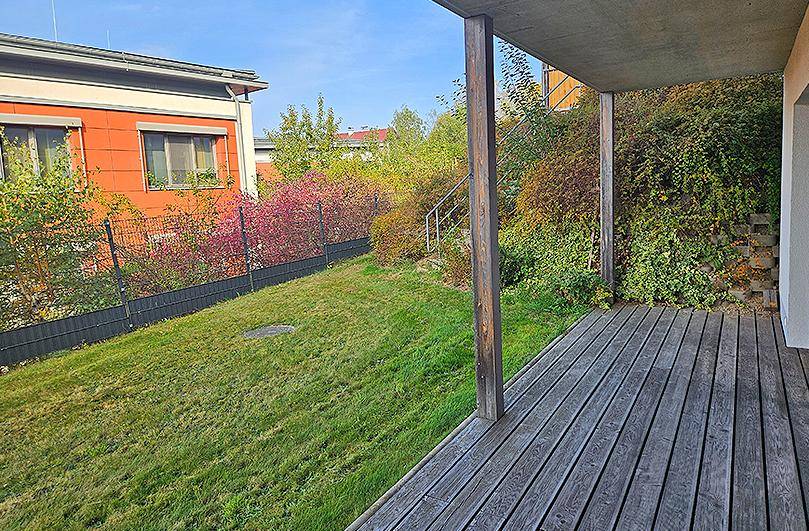 Große Holzterrasse mit Blick auf einen gepflegten Rasen und üppige Bepflanzung.