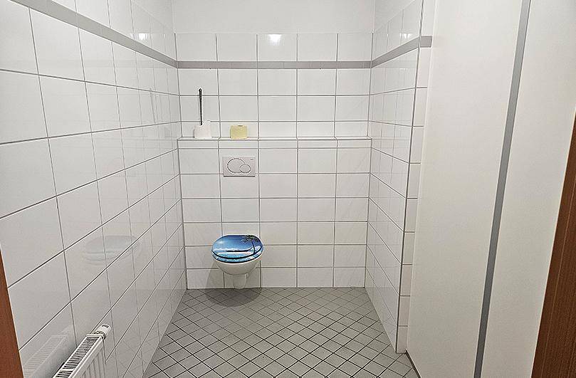Separates WC mit Wand-WC und weißen Fliesen an Wänden und auf dem Boden.