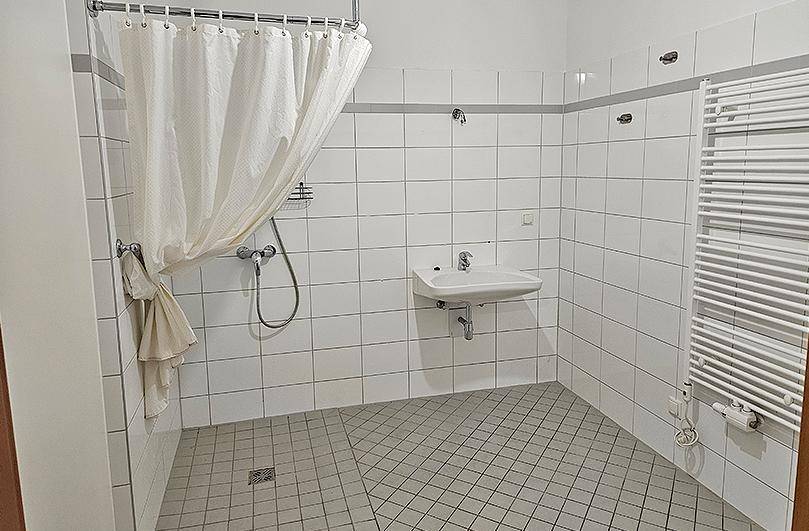 Funktionales Badezimmer mit Duschbereich, Waschbecken und einem beheizten Handtuchhalter.