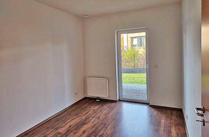 Leerer Raum mit Laminatboden und einer Tür, die direkten Zugang zum Garten bietet.