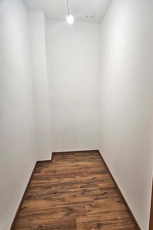 Kleiner, leerer Abstellraum mit Laminatboden und weiß gestrichenen Wänden.