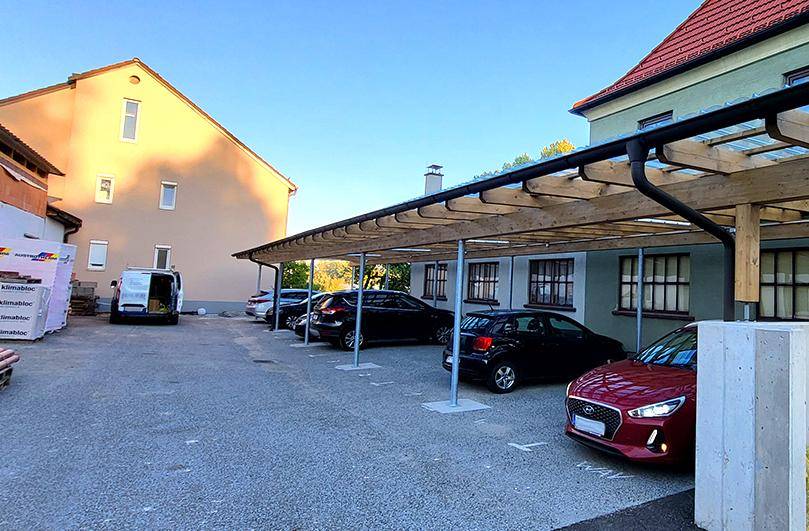 Außenbereich mit überdachten Parkplätzen unter einem Carport und weiteren Stellflächen.