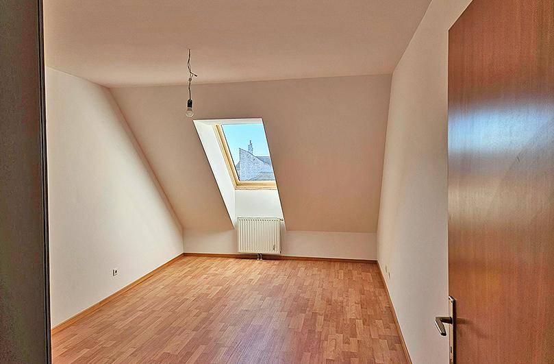 Helles Schlafzimmer im Dachgeschoss mit Holzboden und einem schrägen Dachfenster.