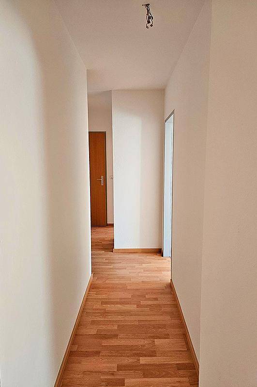 Langer, heller Flur mit Holzboden und weißen Wänden, der zu weiteren Räumen führt.