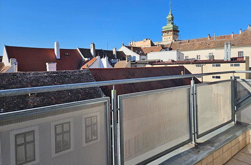 Sonniger Balkon mit Blick über die Dächer der Stadt und einen historischen Kirchturm.