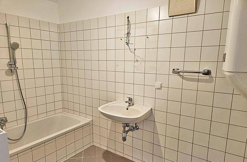 Badezimmer mit Badewanne, Waschbecken und weißen Wandfliesen, bereit zur Modernisierung.