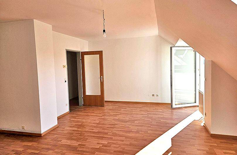 Heller Wohnraum im Dachgeschoss mit Holzboden und Zugang zu einem sonnigen Außenbereich.