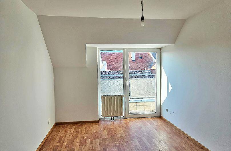 Geräumiger, heller Raum im Dachgeschoss mit Holzboden und Zugang zu einem Balkon.