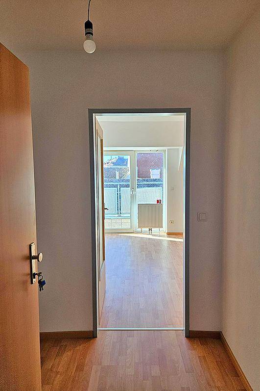 Heller Flur mit Holzboden, der den Blick auf einen sonnigen Raum mit Balkonzugang freigibt.