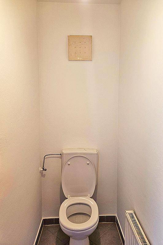 Kleines Gäste-WC mit Toilette, Fliesenboden und Heizkörper.