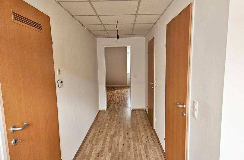 Langer Flur mit mehreren Holztüren und einem Rasterdecken-Design.