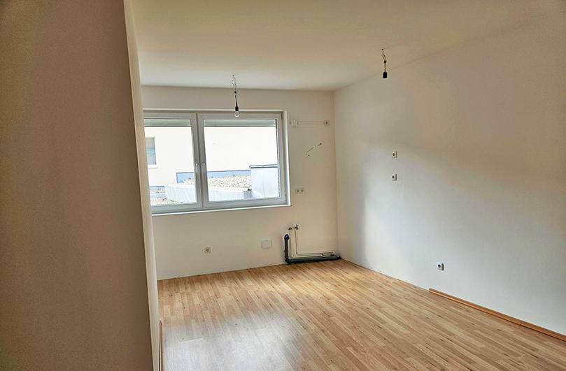 Heller Raum mit Laminatboden und Fenster, vorbereitet für eine Kücheninstallation.