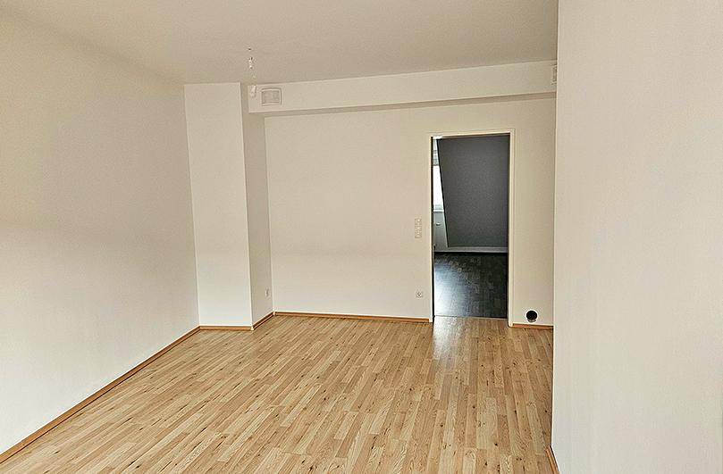Leerer Wohnraum mit hellem Laminatboden und Zugang zu einem weiteren Zimmer.