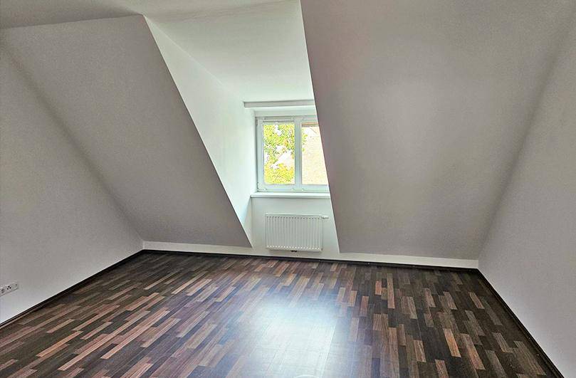 Dachgeschosszimmer mit dunklem Laminatboden, schrägen Wänden und einem Fenster.