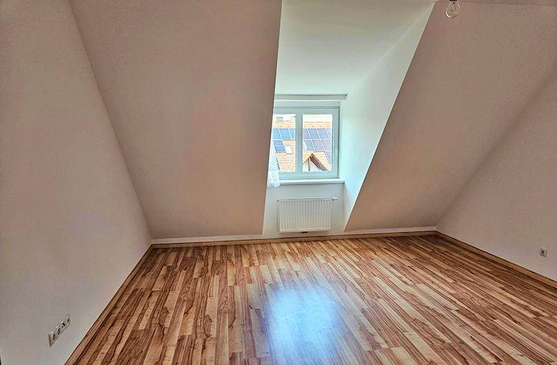 Dachgeschosszimmer mit dunklem Laminatboden, schrägen Wänden und Blick auf Solarpaneele.