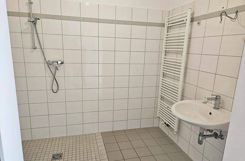 Modern gefliestes Badezimmer mit ebenerdiger Dusche, Waschbecken und Handtuchheizkörper.