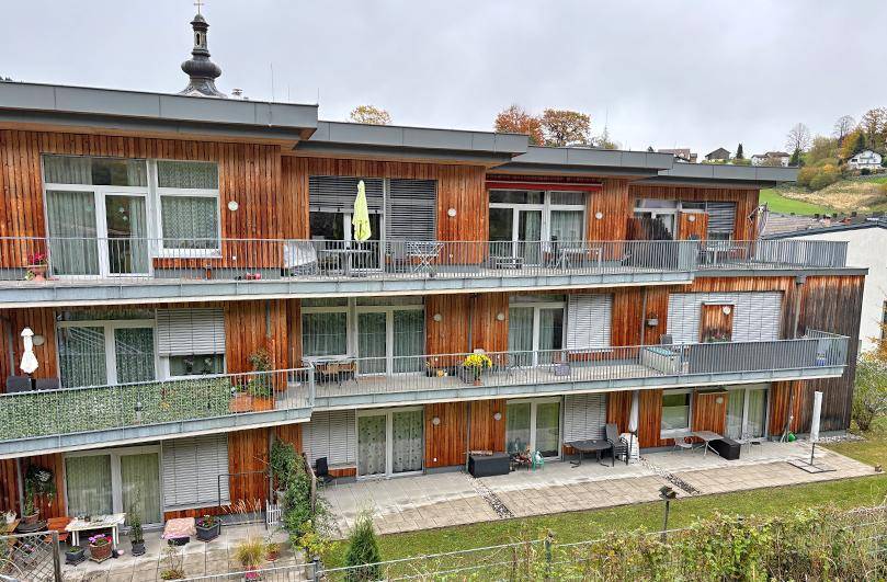 Fassade eines modernen Wohngebäudes mit Holzverkleidung, mehreren Balkonen und Außenjalousien.
