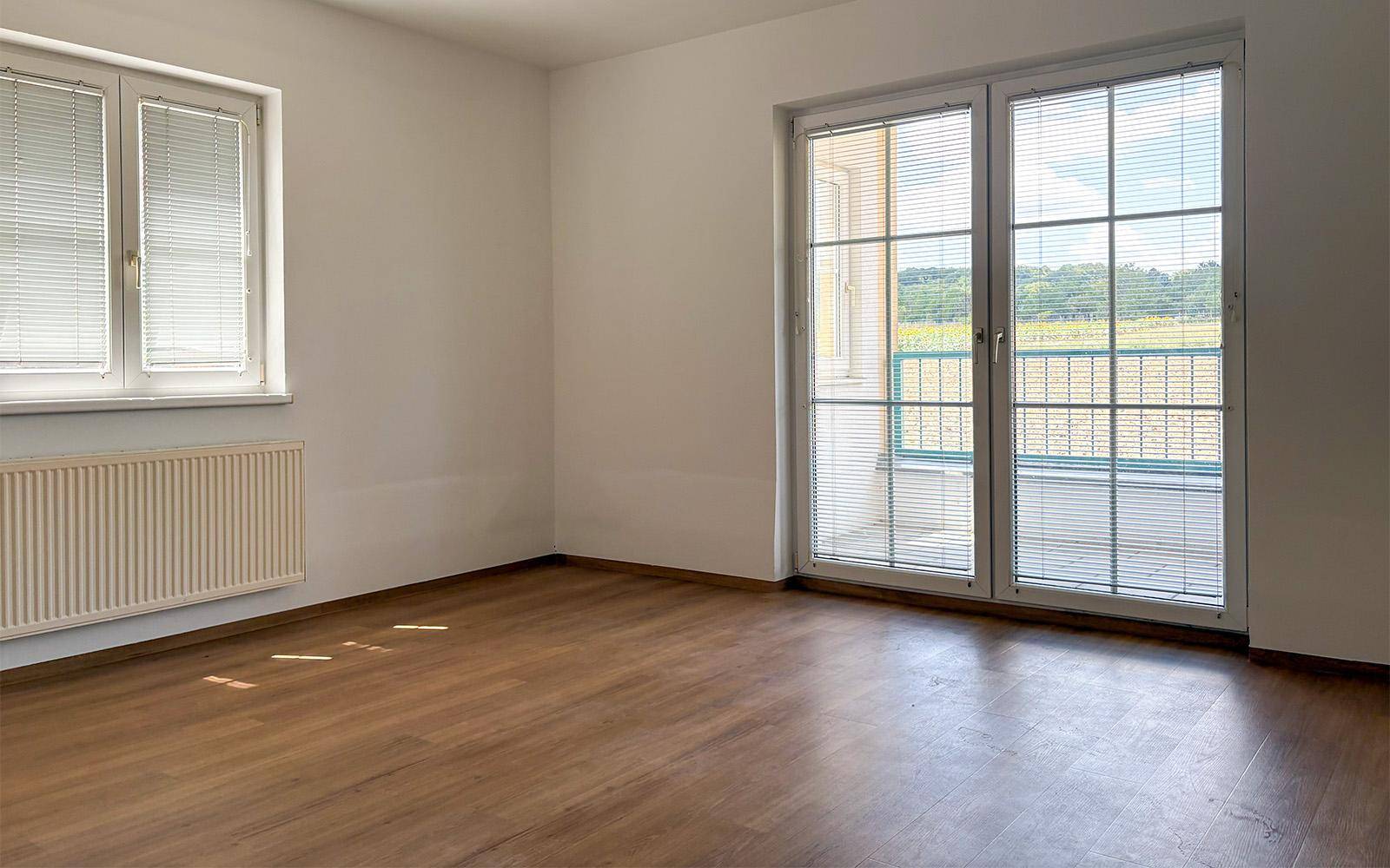 Geräumiges Wohnzimmer mit Laminatboden und großem Fenster mit Zugang zu einem Außenbereich.
