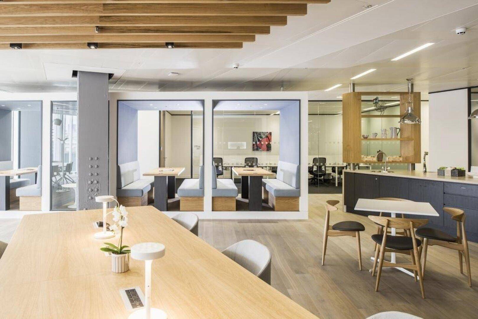 Helles, modernes Büro mit verschiedenen Arbeitsbereichen, Holzboden und dekorativen Deckenbalken.