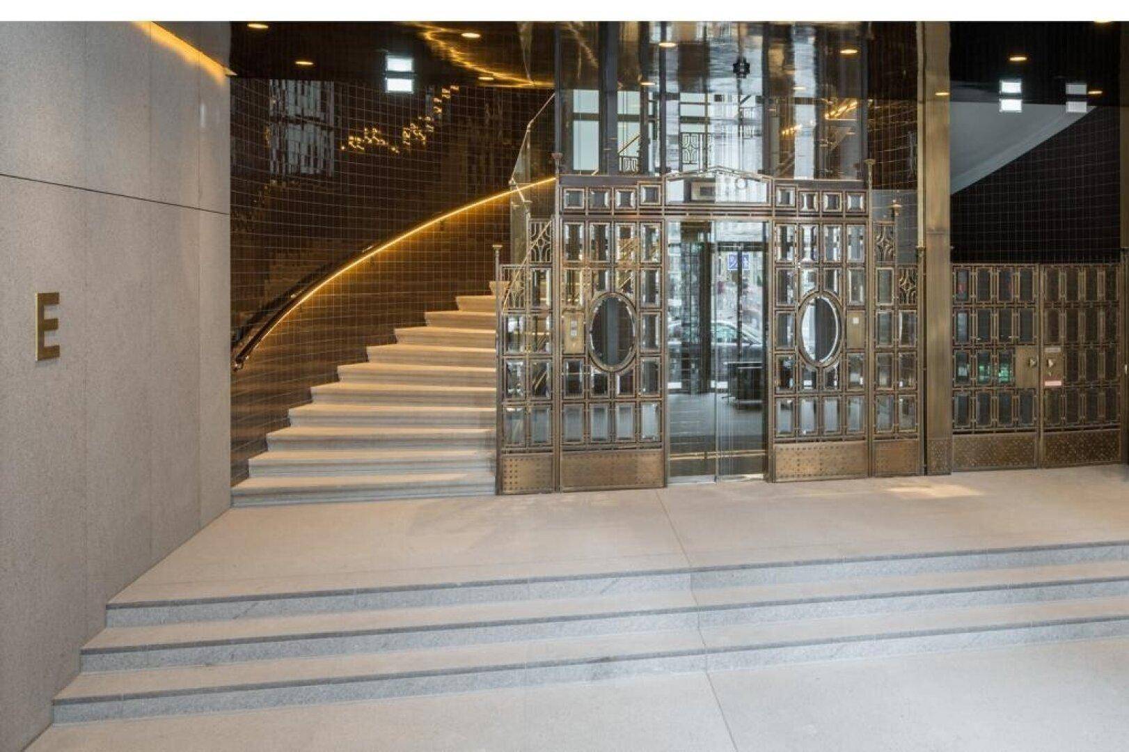 Elegante Eingangshalle mit geschwungener Treppe, glänzenden Oberflächen und einem luxuriösen Aufzug.