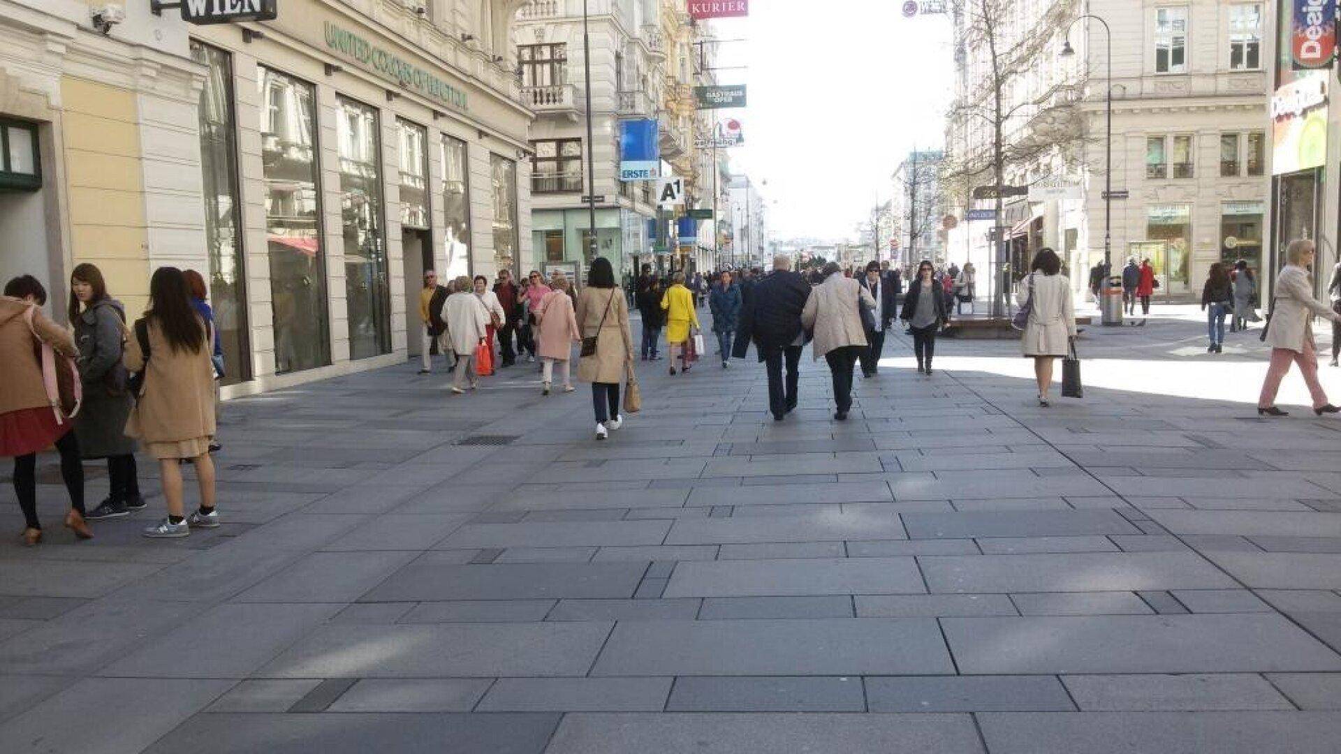Belebte Fußgängerzone mit vielen Passanten, Geschäften und historischen Gebäuden unter strahlendem Sonnenschein.