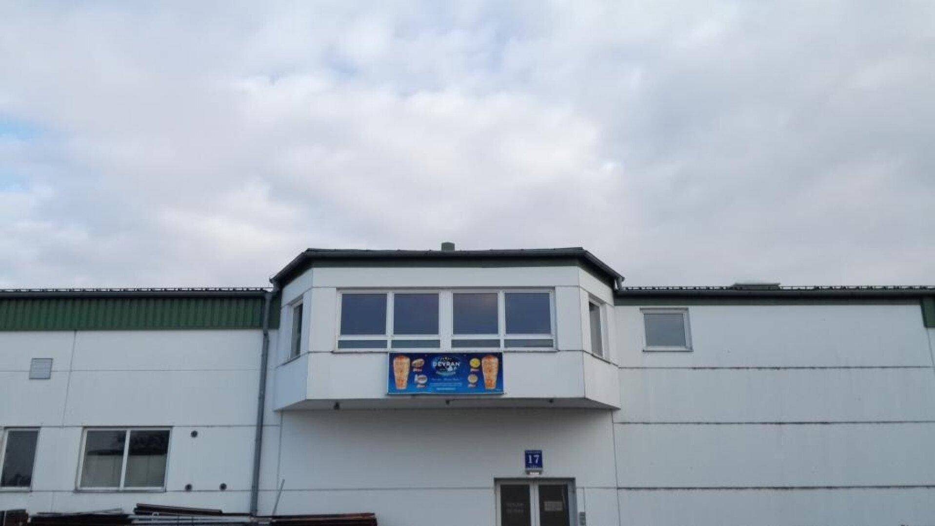 Fassade eines Gebäudes mit Erkerfenstern und einem Werbeschild unter bewölktem Himmel.
