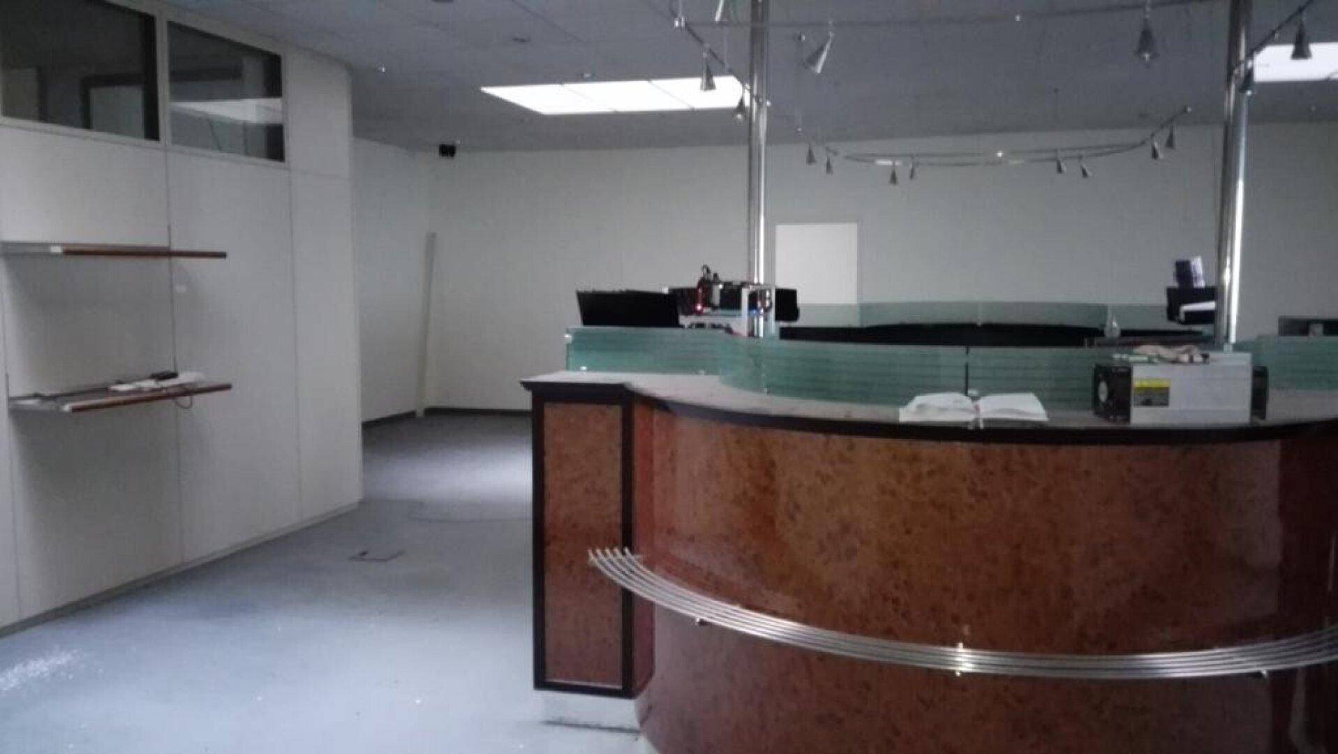 Empfangsbereich oder offener Büroraum mit Holztheke, Glasabtrennung und Schienenbeleuchtung.