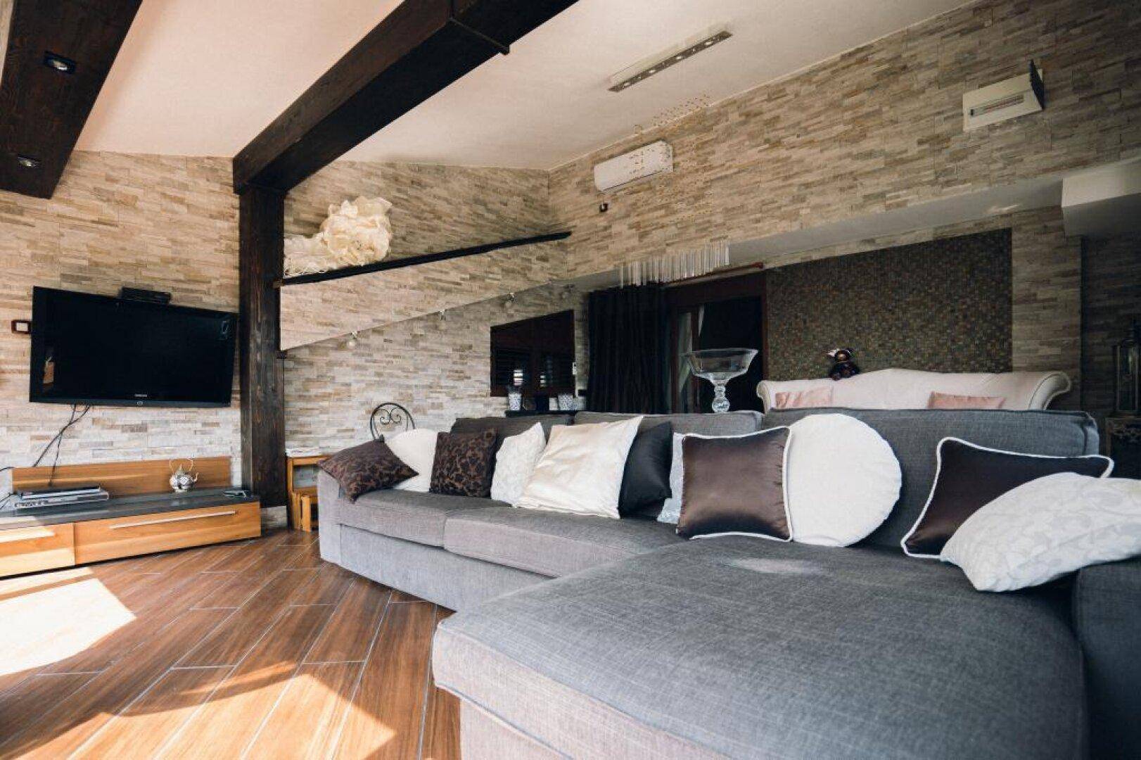 Gemütliches Wohnzimmer mit großem Ecksofa, Holzbalken und Steinwandverkleidung.