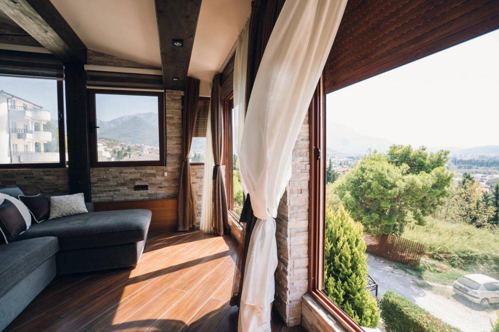 Lichtdurchflutetes Wohnzimmer mit Panoramablick auf die grüne Landschaft und die Berge.