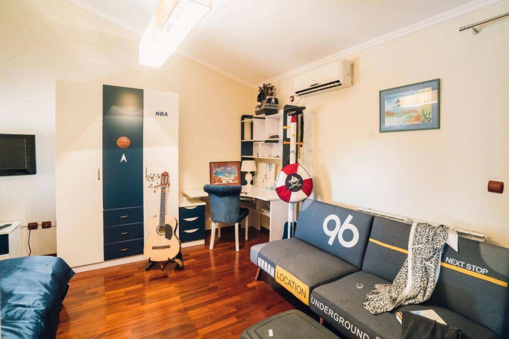Jugendzimmer mit Schlafsofa, Schreibtisch, Kleiderschrank und Holzboden.