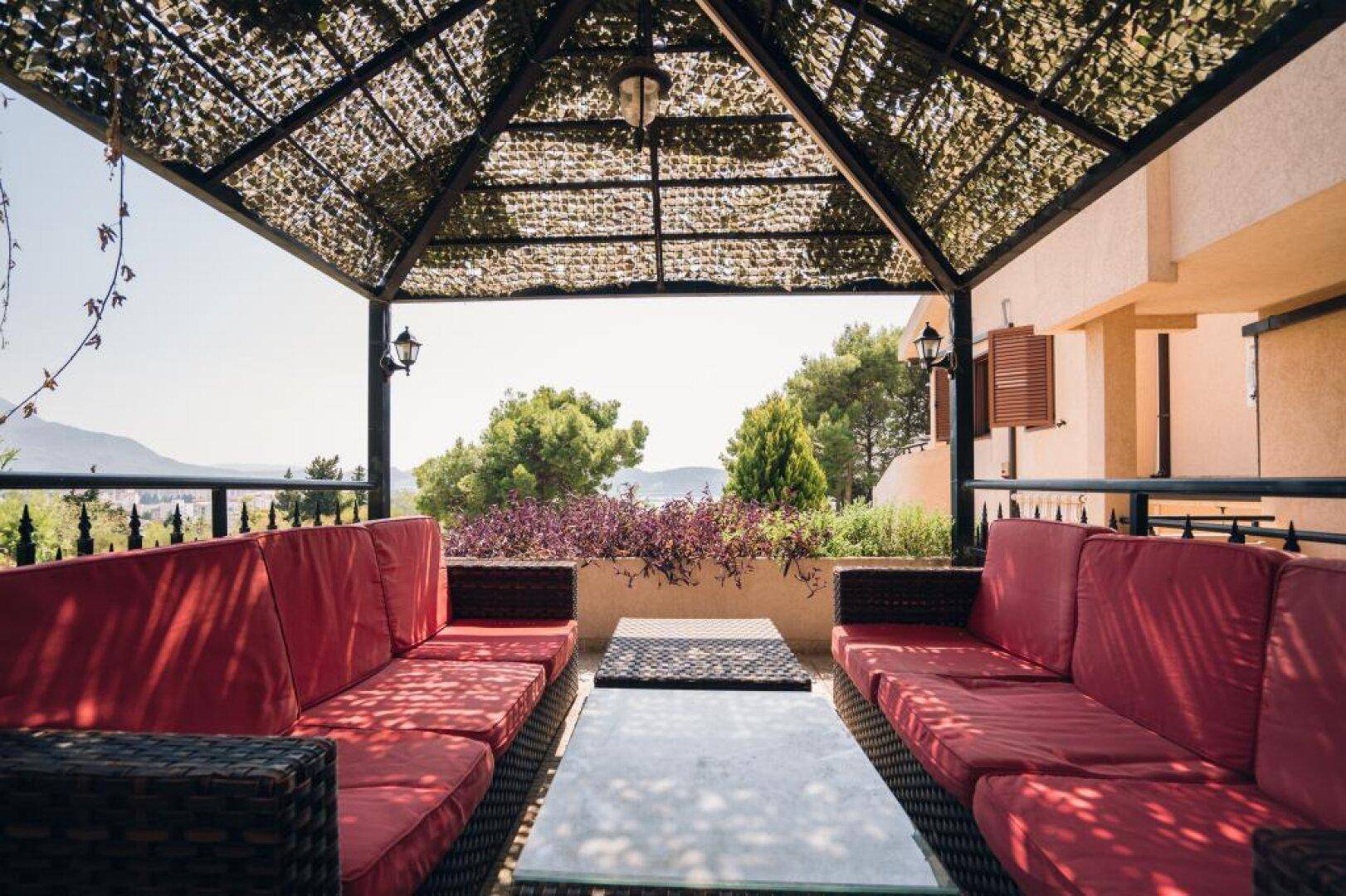 Gemütliche überdachte Terrasse mit bequemen roten Sofas und Blick ins Grüne.