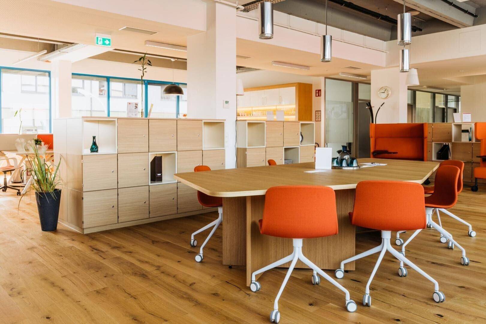 Geräumiger Konferenzraum mit Holztisch, orangefarbenen Stühlen und Pflanzenakzenten.