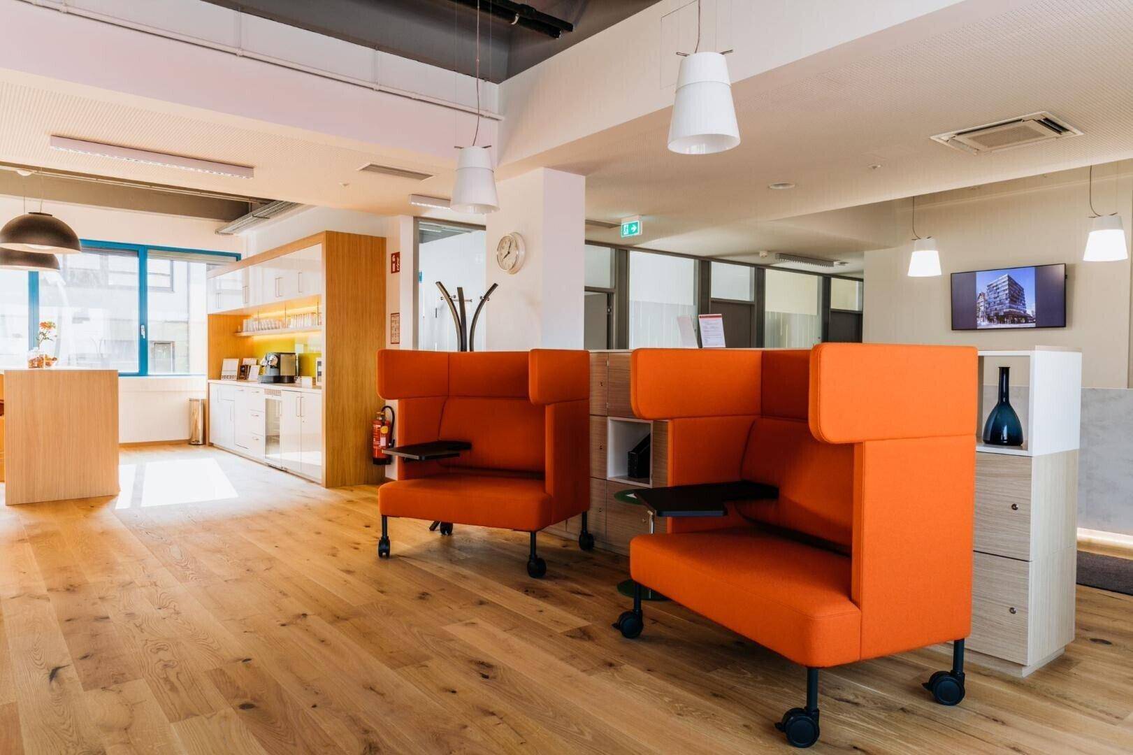 Gemütlicher Loungebereich im Büro mit orangefarbenen Sesseln, Holzboden und offener Gestaltung.