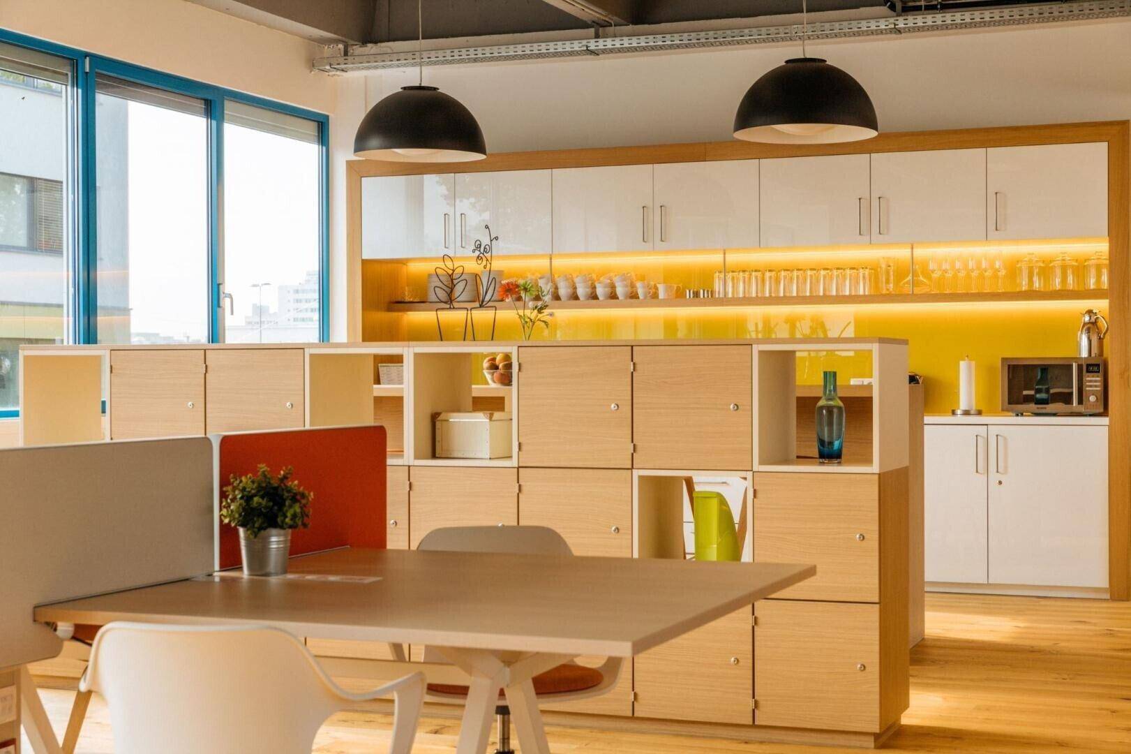 Offener Bürobereich mit integrierter Küche, Holzboden und modularen Schränken für effizientes Arbeiten.