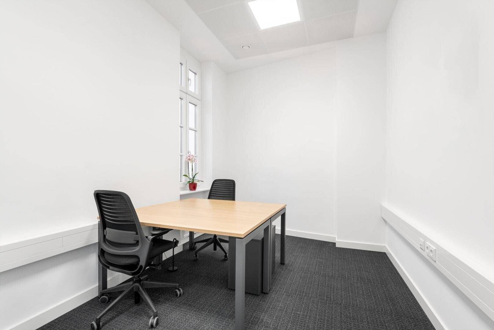 Kompaktes Einzelbüro mit Teppichboden, Schreibtisch und einem Fenster, das für natürliches Licht sorgt.